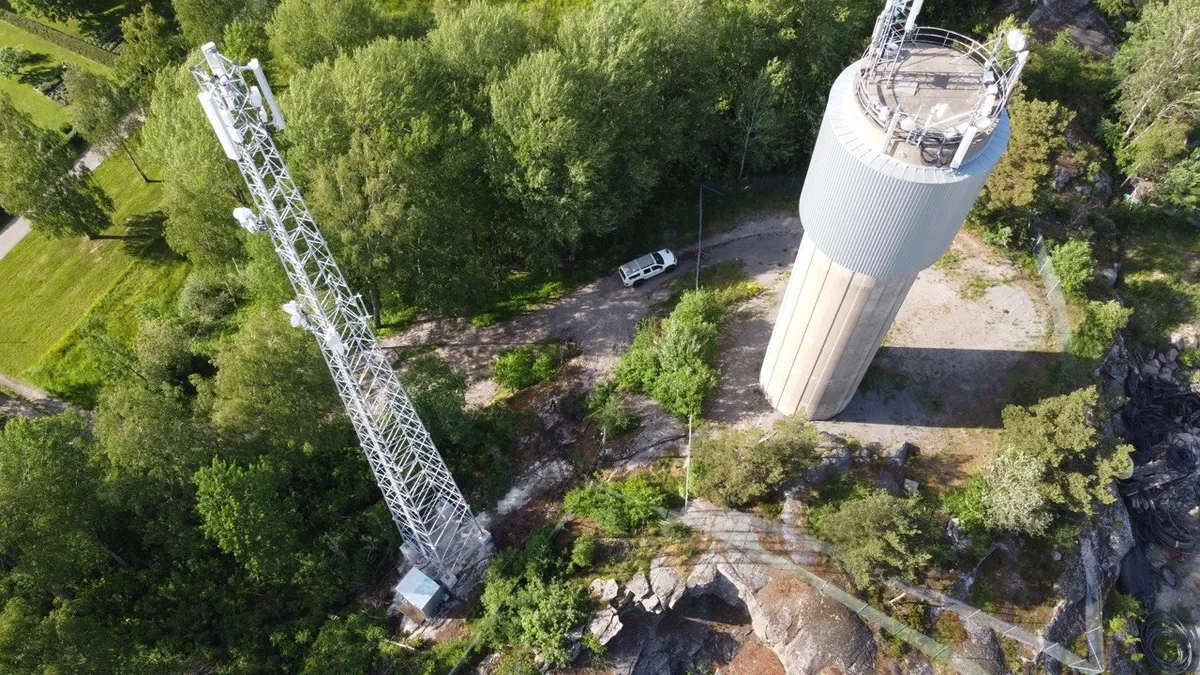 Aerial view of a lattice tower beside a water tower that carries telecom equipment on its roof