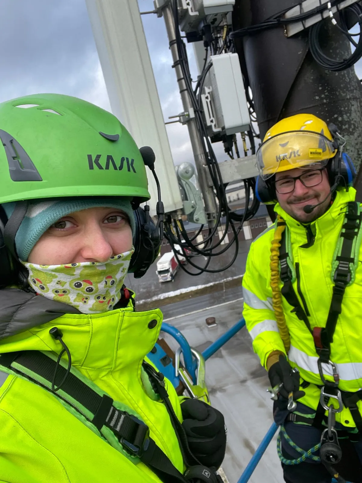 Two technicians in harnesses working at a rooftop antenna mast