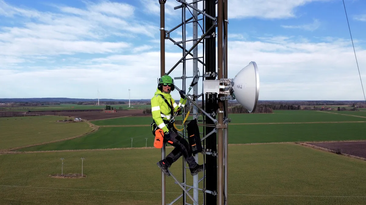 Rigger on a lattice tower next to a newly mounted microwave dish