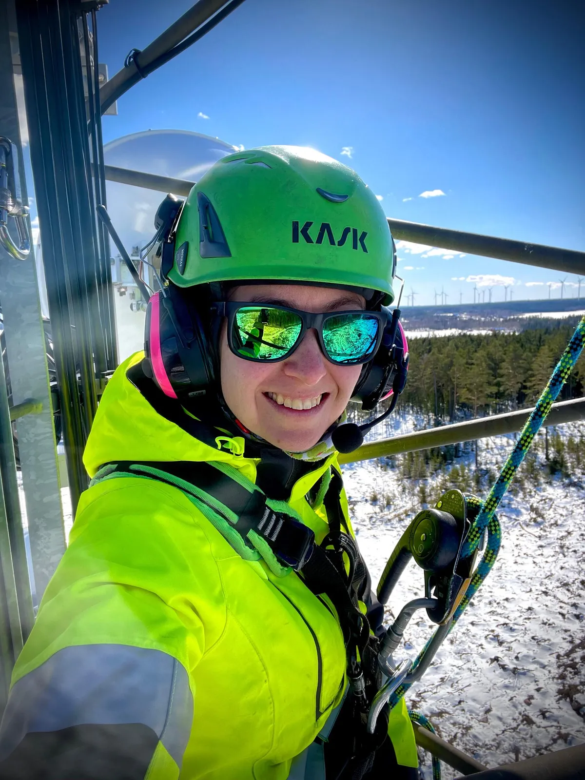 Technician secured to a tower in winter, wind farm in the background